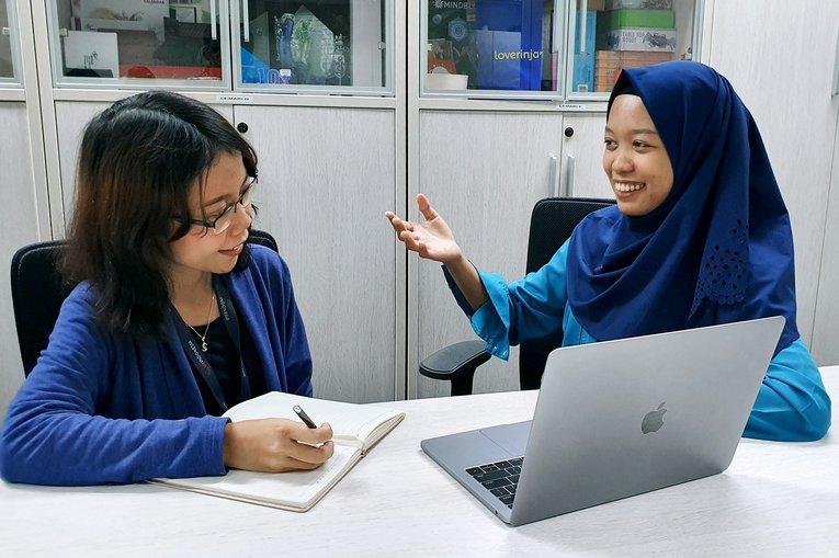 Two people in a room, one looking at the other, and the other looking at a computer